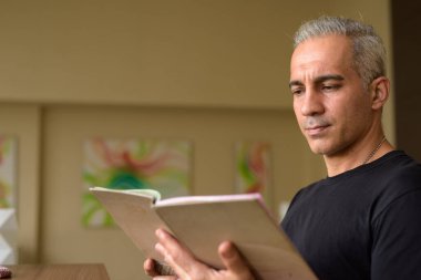 Portrait of handsome Persian man with gray hair at the library inside modern building