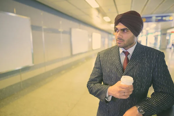 Portrait of young handsome Indian Sikh businessman wearing turban while exploring the city of Bangkok, Thailand