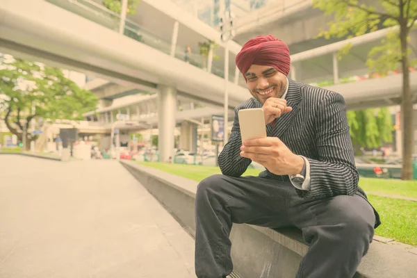 Portrait of young handsome Indian Sikh businessman wearing turban while exploring the city of Bangkok, Thailand