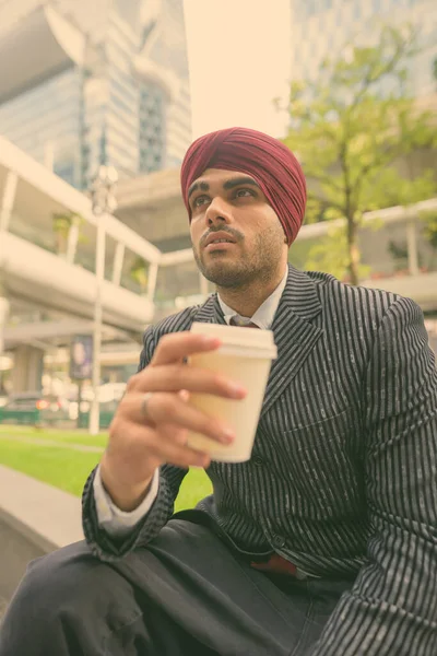 Portrait of young handsome Indian Sikh businessman wearing turban while exploring the city of Bangkok, Thailand