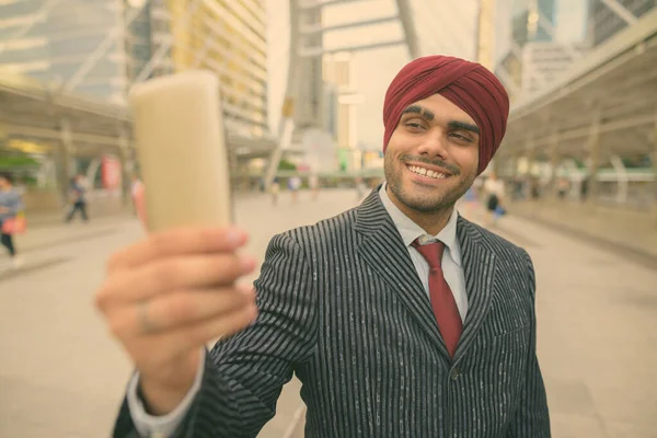 Portrait of young handsome Indian Sikh businessman wearing turban while exploring the city of Bangkok, Thailand
