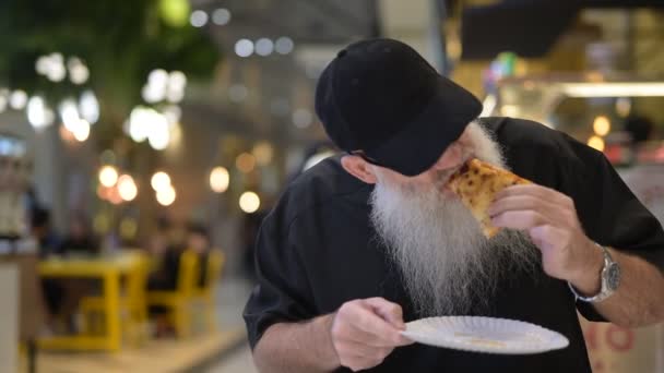 Mann sitzt in Einkaufszentrum und isst Pizza — Stockvideo