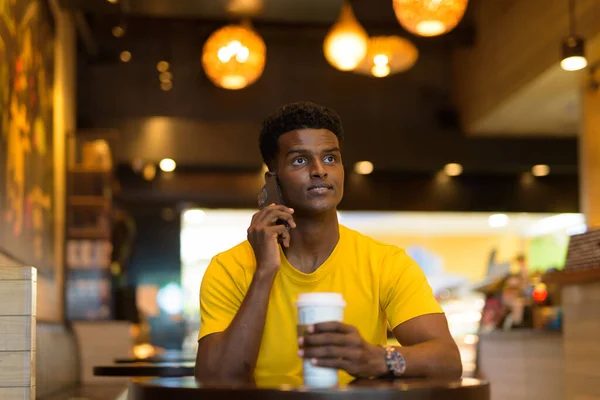 Portrait of handsome black African man wearing yellow t-shirt outdoors in city in Bangkok, Thailand