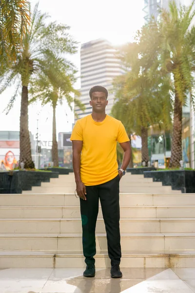 Portrait of handsome black African man wearing yellow t-shirt outdoors in city in Bangkok, Thailand