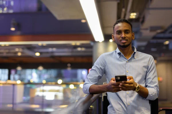 Portrait of handsome black African businessman inside shopping mall using mobile phone horizontal shot