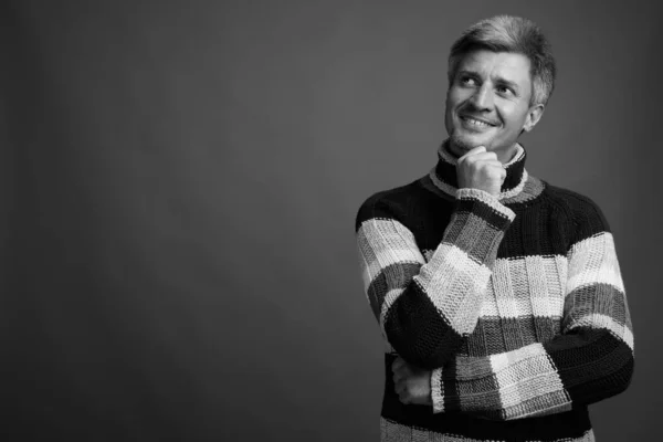 Studio shot of man with blond hair wearing turtleneck sweater against gray background in black and white