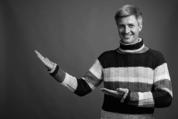 Studio shot of man with blond hair wearing turtleneck sweater against gray background in black and white