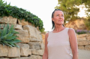 Portrait of a mature woman standing in front of a stone wall looking away