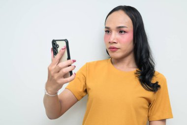 Telefon kullanarak uzun saçlı, makyajlı Taylandlı genç bir transseksüelin stüdyo portresi. Cinsiyet ifadesi kavramı, LGBTQ gururu ve özgün güzellik ve çeşitliliği gösteren kapsayıcılık.
