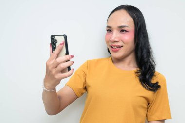 Telefon kullanarak uzun saçlı, makyajlı Taylandlı genç bir transseksüelin stüdyo portresi. Cinsiyet ifadesi kavramı, LGBTQ gururu ve özgün güzellik ve çeşitliliği gösteren kapsayıcılık.