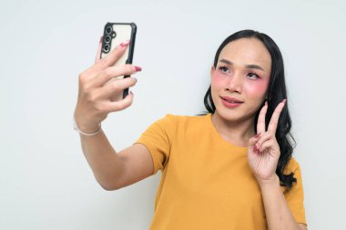 Telefon kullanarak uzun saçlı, makyajlı Taylandlı genç bir transseksüelin stüdyo portresi. Cinsiyet ifadesi kavramı, LGBTQ gururu ve özgün güzellik ve çeşitliliği gösteren kapsayıcılık.