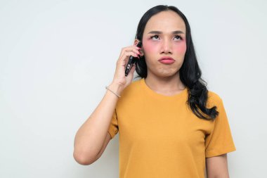Telefon kullanarak uzun saçlı, makyajlı Taylandlı genç bir transseksüelin stüdyo portresi. Cinsiyet ifadesi kavramı, LGBTQ gururu ve özgün güzellik ve çeşitliliği gösteren kapsayıcılık.