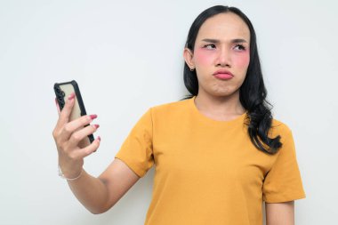 Telefon kullanarak uzun saçlı, makyajlı Taylandlı genç bir transseksüelin stüdyo portresi. Cinsiyet ifadesi kavramı, LGBTQ gururu ve özgün güzellik ve çeşitliliği gösteren kapsayıcılık.