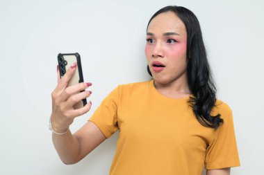 Telefon kullanarak uzun saçlı, makyajlı Taylandlı genç bir transseksüelin stüdyo portresi. Cinsiyet ifadesi kavramı, LGBTQ gururu ve özgün güzellik ve çeşitliliği gösteren kapsayıcılık.