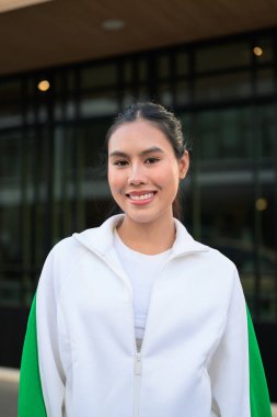 Açık havada spor giyimli mutlu bir Asyalı kadın. Neşeli ifade, doğal ışık ve refah, canlılık ve zindelik temaları için pozitif enerji içeren günlük yaşam tarzı portresi.