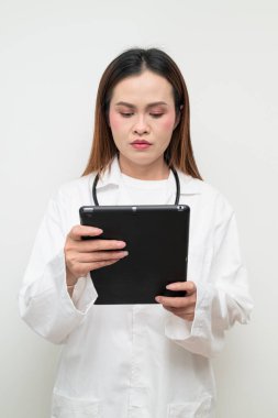 Tablet bilgisayar kullanan, beyaz önlük ve steteskop giyen Asyalı bir sağlık uzmanının stüdyo portresi. Tıbbi, hastane, klinik ve sağlık konularına uygun kavram.