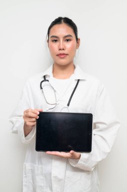 Beyaz üniformalı genç bir Taylandlı kadın doktorun portresi, arka planda steteskop bulunan dijital tablet bir bilgisayar kullanıyor, sağlık reklamcılığı veya tıbbi iletişim için uygun..