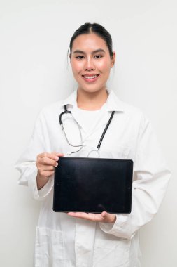 Beyaz üniformalı genç bir Taylandlı kadın doktorun portresi, arka planda steteskop bulunan dijital tablet bir bilgisayar kullanıyor, sağlık reklamcılığı veya tıbbi iletişim için uygun..