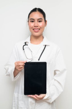Beyaz üniformalı genç bir Taylandlı kadın doktorun portresi, arka planda steteskop bulunan dijital tablet bir bilgisayar kullanıyor, sağlık reklamcılığı veya tıbbi iletişim için uygun..