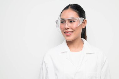 Koruyucu gözlük takan kadın bir bilim adamının portresi ve temiz bir stüdyo geçmişine sahip beyaz bir laboratuvar önlüğü. Bilim, laboratuvar çalışmaları, araştırma, güvenlik ve STEM temaları için elverişli.