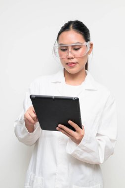 Koruyucu gözlük takan kadın bir bilim adamının portresi ve temiz bir stüdyo geçmişine sahip beyaz bir laboratuvar önlüğü. Bilim, laboratuvar çalışmaları, araştırma, güvenlik ve STEM temaları için elverişli.