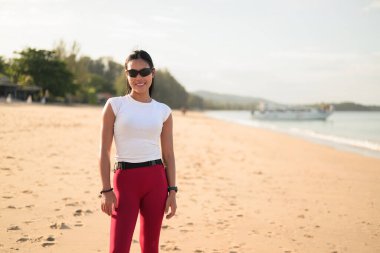 Spor kıyafetli genç Asyalı kadın yaz aylarında plajda spor salonunda dikiliyor.