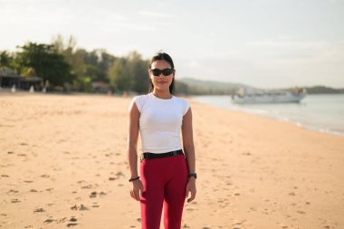 Spor kıyafetli genç Asyalı kadın yaz aylarında plajda spor salonunda dikiliyor.