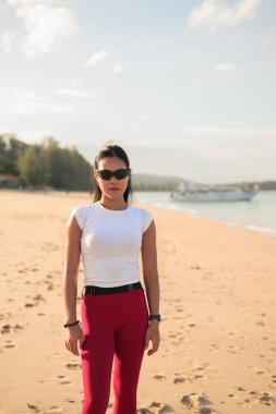 Spor kıyafetli genç Asyalı kadın yaz aylarında plajda spor salonunda dikiliyor.