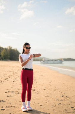 Spor kıyafetli genç Asyalı kadın yaz aylarında plajda spor salonunda dikiliyor.