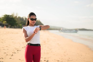 Spor kıyafetli genç Asyalı kadın yaz aylarında plajda spor salonunda dikiliyor.