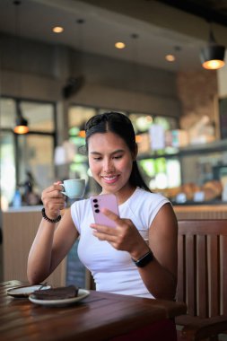 Gülümseyen Kadın Espresso ve Çikolatalı Pastayı Telefonla Kullanırken Kafe Restoranında Keyfini Çıkarıyor