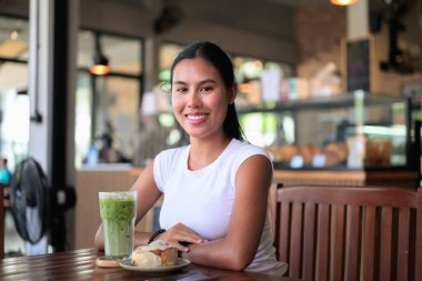 Gülümseyen Asyalı Kadın Buzlu Matcha Latte içiyor Cafe with Tatlıyla