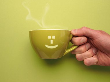 Turuncu arka planda gülümseyen bir ikonu olan yeşil kahve kupası güne iyi bir başlangıç yap.