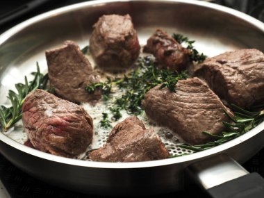 Taze biberiyeli organik biftek filetosu ve paslanmaz çelik bir tavada kekik, yukarıdan bakıldığında taze otlar, organik yiyecekler veya sağlıklı beslenme konseptiyle pişirilmiş.