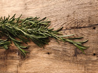 Kırsal ahşap mutfak masasında organik biberiye dalı, sağlıklı yemek veya malzeme konsepti.