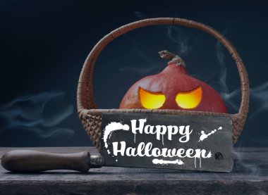 Cadılar bayramı balkabağı Jack o Lantner 'ı bir sepetin içine oymuş. Kasap satırıyla birlikte ahşap bir masada. Mesaj için yer var.