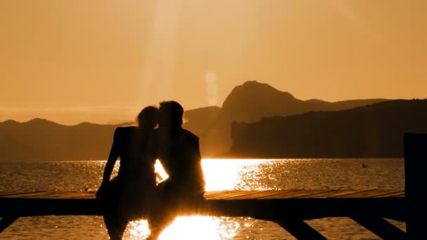 Hombre y mujer sentados en el puente al atardecer — Vídeos de Stock