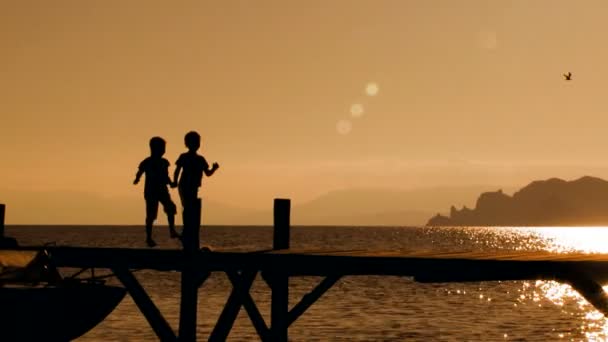 Двое детей бегут по мосту на закате — стоковое видео