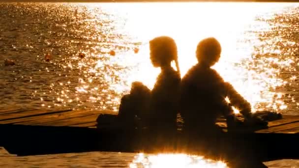 Маленький хлопчик і дівчинка сидить на мосту на заході сонця — стокове відео