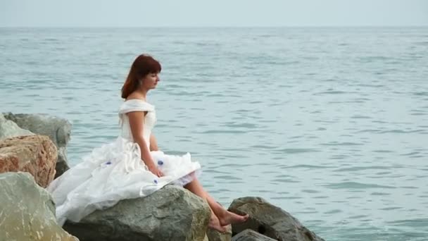 Mujer hermosa sentada en la roca por el mar — Vídeos de Stock