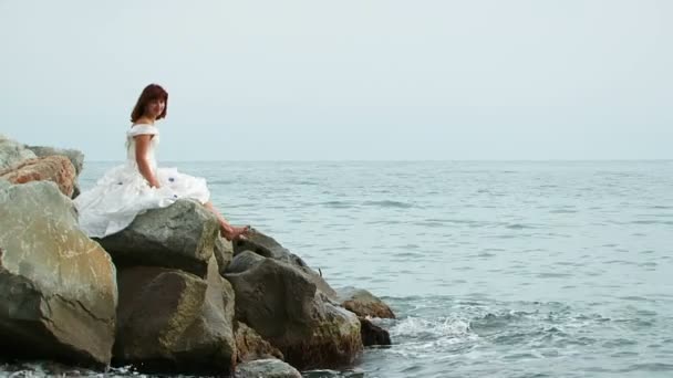 Mooie vrouw In witte jurk zittend op Rock door zee — Stockvideo