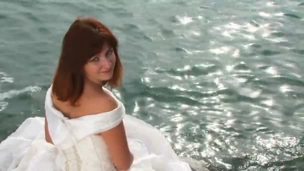 Mujer bonita joven en vestido blanco sentado en la roca por el mar — Vídeos de Stock