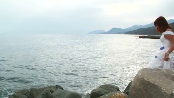 Chica joven en vestido blanco de pie en la roca por el mar — Vídeos de Stock