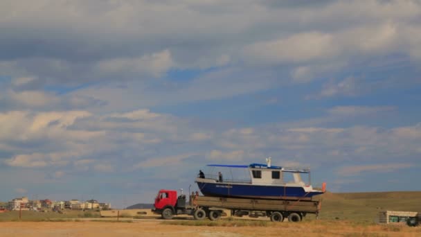 Redactionele. Grote vrachtwagen met zeilboot aan boord langs de kust — Stockvideo