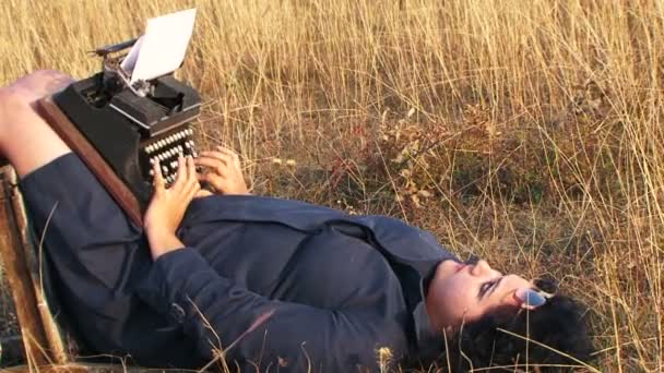Mulher engraçada digitando na máquina de escrever vintage deitado na cadeira na natureza — Vídeo de Stock