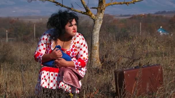 Mujer extraña en blanco vestido de punto sentado cerca de la maleta en la naturaleza — Vídeo de stock