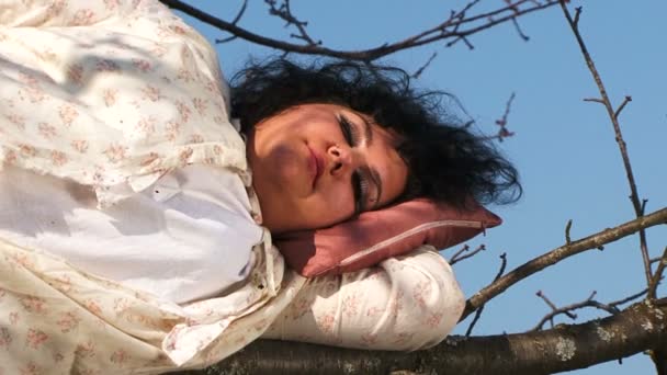 Темноволосая женщина в длинной белой ночной рубашке, спящая на дереве — стоковое видео