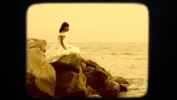 Mujer joven en vestido blanco sentado en la roca por el mar — Vídeo de stock