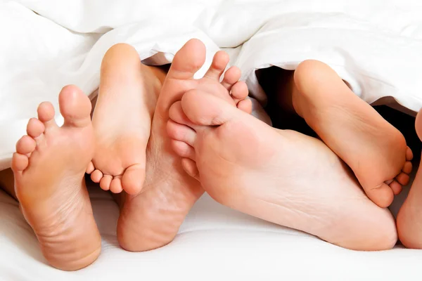 Suelas de una familia en la cama bajo las sábanas . — Foto de Stock