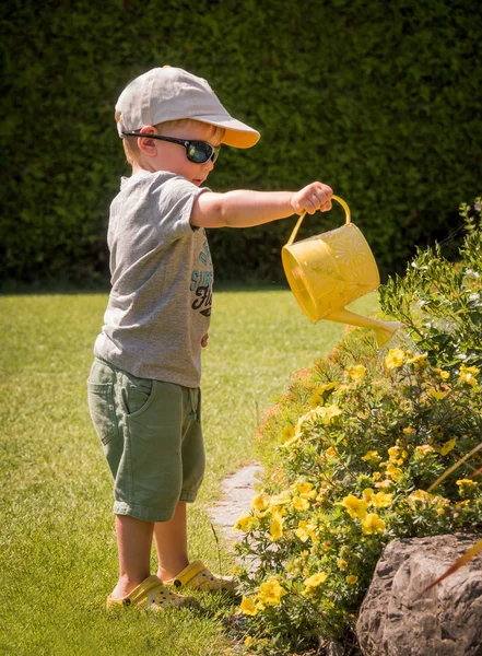 Little boy with a can watering flowers in summer — Stock Photo, Image